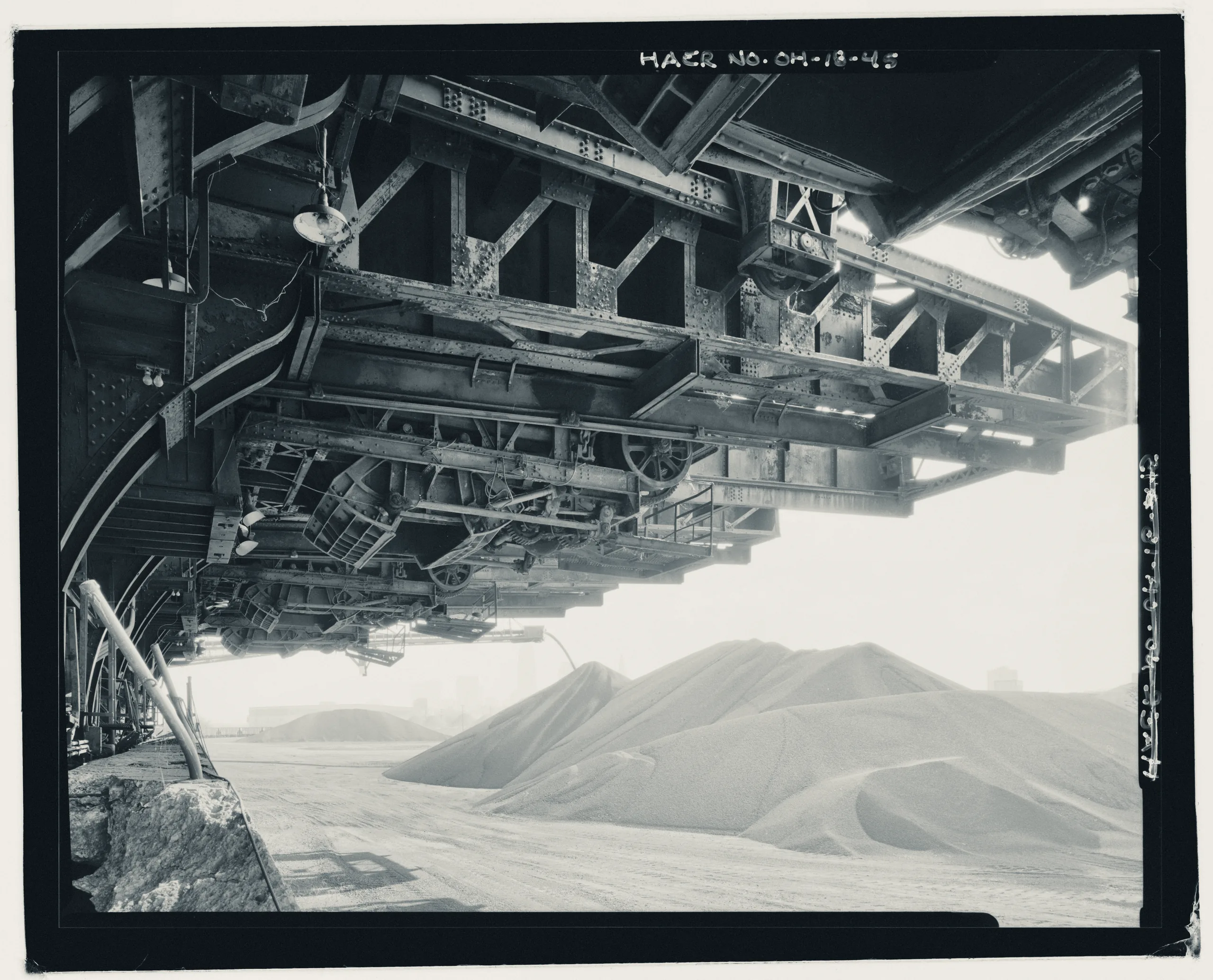CONTEXT VIEW FROM UNDER REAR OF HULETTS LOOKING OUT INTO THE ORE YARD FILLED WITH ORE, SHOWING SELF-UNLOADING SHIP BOOM IN ACTION. LOOKING EAST. - Pennsylvania Railway Ore Dock